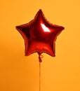 Single big red star metallic balloon ballon object for birthday party on dark yellow Royalty Free Stock Photo