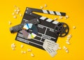 Single, black, open movie clapper or clapper-board with dvd movie disc, film reel, popcorn, remote control and movie theatre Royalty Free Stock Photo