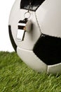 Single black and white soccer sports ball with referee whistle close up with selective focus on green grass over white