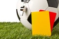 Single black and white soccer sports ball with referee whistle and yellow and red referee cards with selective focus on green