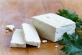 Single block of white tofu with two tofu slices, crumbs and fresh parsley on wooden chopping board.