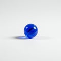 A single blue glass marble sits on a plain white surface. The marble is spherical and Royalty Free Stock Photo