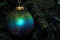 A single blue and green, round Christmas ornament with gold sparkles hanging on a Christmas tree Royalty Free Stock Photo