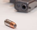 A single bullet on a white table with a black pistol in the background Royalty Free Stock Photo