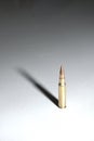 A single bullet 7.62 x 51 mm NATO standing on a white surface with long dramatic shadow