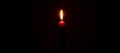 A single burning candle flame or light glowing on red candle on black or dark background on table in church for Christmas, funeral Royalty Free Stock Photo