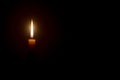 A single burning candle flame or light glowing on a single small yellow candle isolated on black or dark background Royalty Free Stock Photo