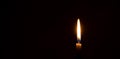 A single burning candle flame or light glowing on a small orange candle on black or dark background on table in church for Royalty Free Stock Photo