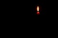 Single burning candle flame or light glowing on a small red candle on black or dark background on table in church for Christmas, Royalty Free Stock Photo