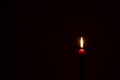 Single burning candle flame or light glowing on a small red candle on black or dark background on table in church for Christmas, Royalty Free Stock Photo