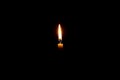 Single burning candle flame or light glowing on a small white candle on black or dark background on table in church for Christmas Royalty Free Stock Photo