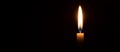 Single burning candle flame or light glowing on a small white candle on black or dark background on table in church for Christmas Royalty Free Stock Photo