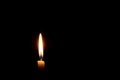 Single burning candle flame or light glowing on a small yellow candle on black or dark background on table in church for Christmas Royalty Free Stock Photo