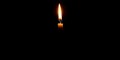 Single burning candle flame or light glowing on a small yellow candle on black or dark background on table in church for Christmas Royalty Free Stock Photo