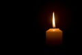 A single burning candle flame or light glowing on a white candle on black or dark background on table in church for Christmas, Royalty Free Stock Photo