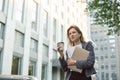 Single calm smiling businesswoman with folded hands walking the street with coffee, documents and laptop. Cheerful young female Royalty Free Stock Photo