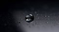 A single, clear droplet rests on a smooth, dark surface. The background is softly Royalty Free Stock Photo