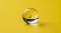 Single clear glass marble with internal bubbles on a bright yellow surface Royalty Free Stock Photo