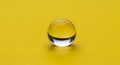 Single clear glass marble resting on a bright yellow textured surface Royalty Free Stock Photo