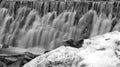 Single clog on snow pile in front of waterfall with many steps in black and white