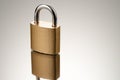 Single closed padlock in gold color on reflective surface. Three-quarter front view