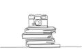 Single continuous line drawing of vintage classic analog pocket camera above stack of books on desk. Old retro photography Royalty Free Stock Photo