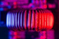 Single copper induction coil with copper wire on electronic PCB close up in red and blue lighting