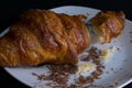 Single croissant on a white plate, dark background, side view