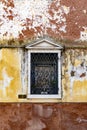 Single crooked window with rusted metal bars on an old semi-destroyed mossy wall in Venice, Italy