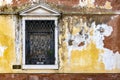 Single crooked window with rusted metal bars on an old semi-destroyed mossy wall in Venice, Italy