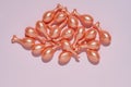 Single-dose serum capsules with active ingredients scattered on a pink background. Skin care and beauty products