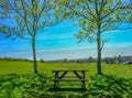 Single empty wooden picnic table set between two trees on grass looking towards view of London