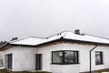 Single-family house roof covered with snow against a cloudy sky. Visible system chimney, doors, windows and falling snow. Royalty Free Stock Photo