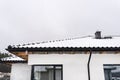 Single-family house roof covered with snow against a cloudy sky. Visible system chimney, roof trusses, windows and falling snow. Royalty Free Stock Photo