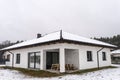 Single-family house roof covered with snow against a cloudy sky. Visible system chimney, roof trusses, windows and falling snow. Royalty Free Stock Photo