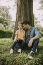 Single father sitting on grass by the tree with little daughter Royalty Free Stock Photo