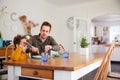 Single Father Sitting At Table Eating Meal With Son In Kitchen At Home