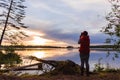 A single figure of traveller taking a photo of wonderful landscape. Beautiful forest lake in sunset rays. Travel and camping