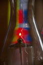 A single flame burns inside an oil lamp with stained glass forming a colorful background