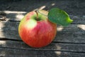 A single fresh red apple with green leaf on old wooden background in sunny day, closeup. Still life from ripe apple for Royalty Free Stock Photo