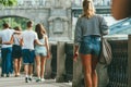 A single girl in short denim shorts, a striped shirt, with a handbag on the background of two couples in love who