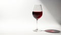 Single glass of deep red wine rests on clean white surface, casting long shadow. Minimalism, elegant design emphasize beverage Royalty Free Stock Photo
