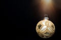 Single glittering golden Christmas tree ornament ball on solid black background. Light glow. New Years greeting card