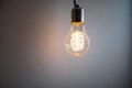 A single glowing light bulb with a coiled filament hanging against a grey background Royalty Free Stock Photo
