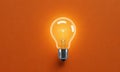 single, glowing light bulb illuminates dark orange background, casting shadow and highlighting its shape and Royalty Free Stock Photo