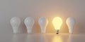 Single glowing light bulb in row of white bulbs over bright background, creativity, uniqueness or standing out concept Royalty Free Stock Photo