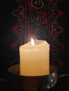 A single glowing pillar candle backed by Chinese handiwork