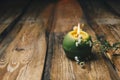 Single green ball-shaped candle with a dry flower burning on a rustic wooden table close-up