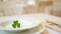 Single green clover leaf centered on stacked white plates at elegant table Royalty Free Stock Photo