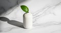 A single green leaf is placed in a small, white ceramic vase on a marble surface. The vase has a Royalty Free Stock Photo